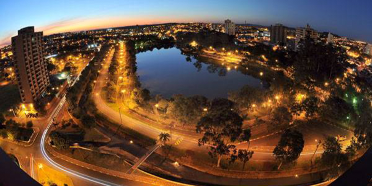 Imagem de cidade com um lago ao centro, cercada de casas e prédios, em dia claro de céu azul. 