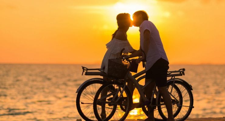 casal com bicicletas a beira mar com pôr do sol ao fundo.