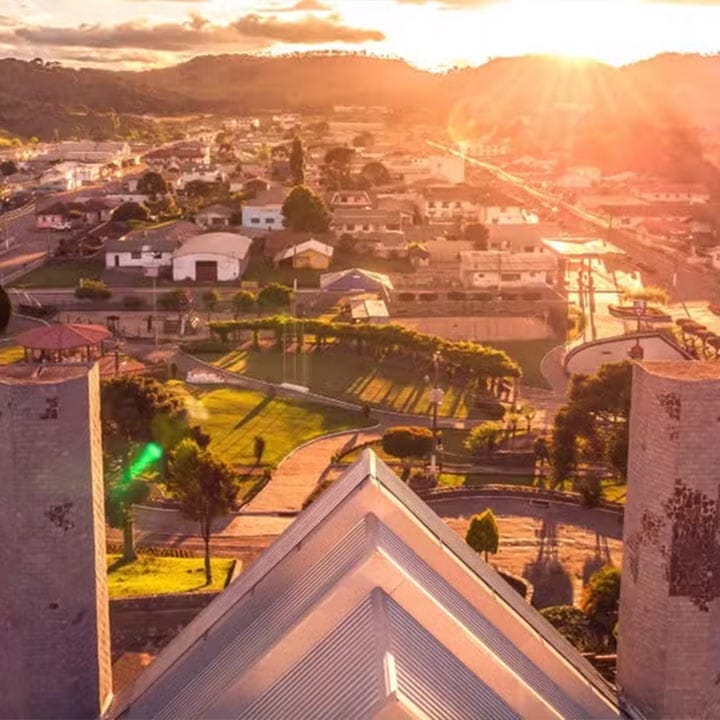 Vista aérea de uma cidade ao pôr do sol, com prédios, parques e ruas bem demarcadas, mostrando a beleza urbana ao entardecer.