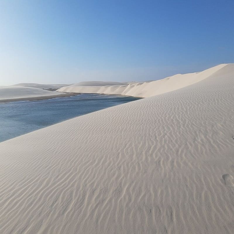 Lençois Maranhenses de areia branca e água azulada sob céu claro, cenário de beleza natural e tranquilidade.